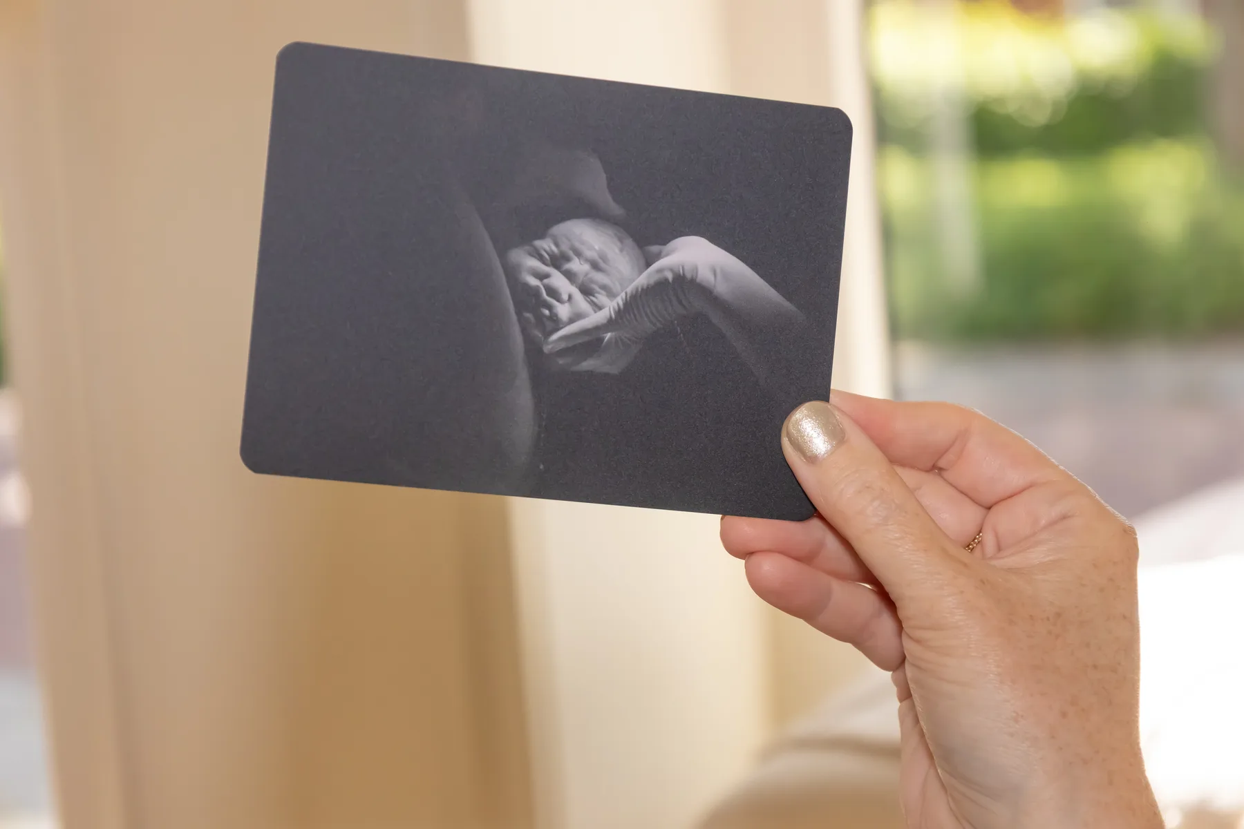 Een hand houdt een zwart-witfoto van een pasgeboren baby vast
