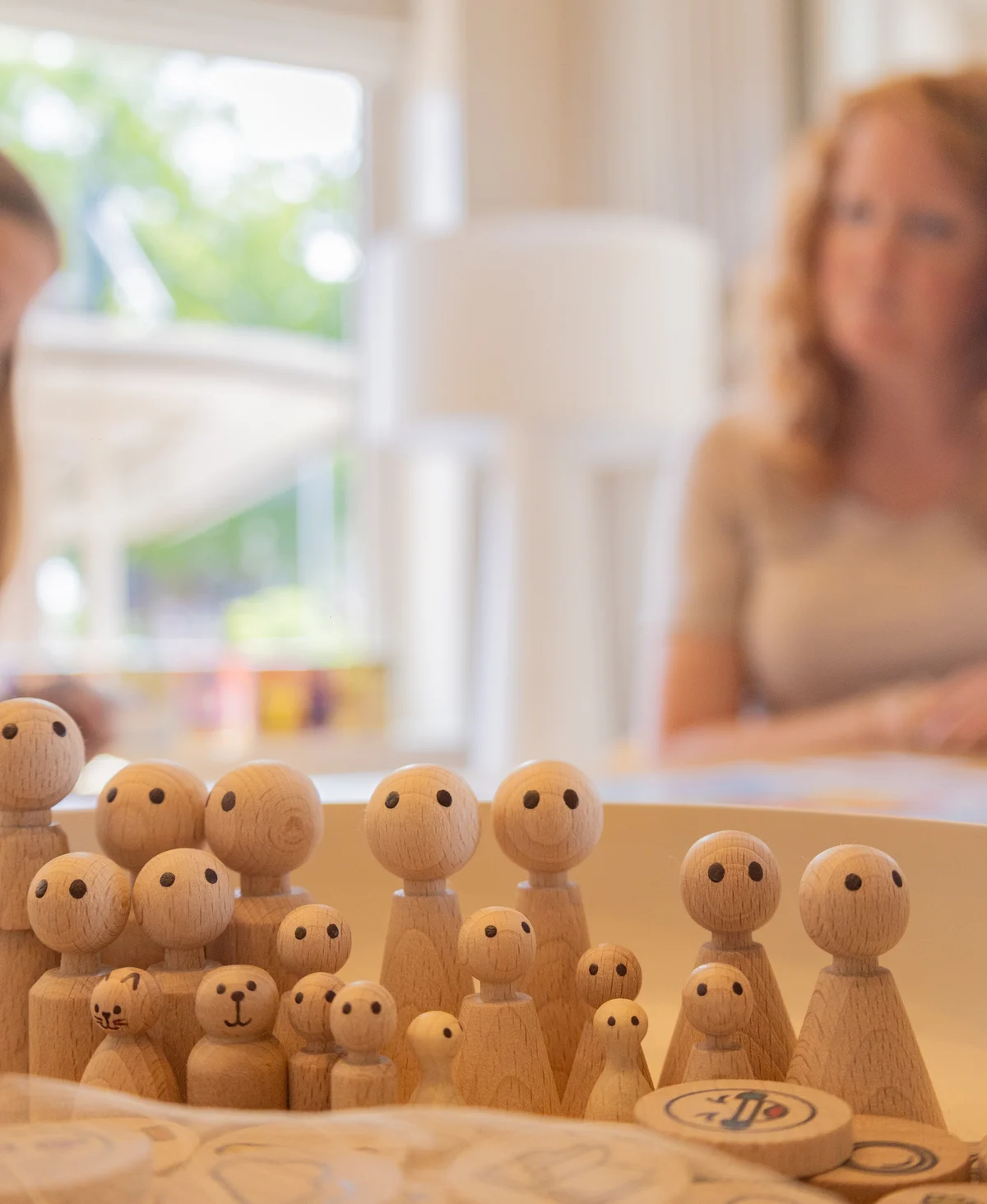 Houten poppetjes op de werktafel in warm daglicht, met een karaf water op de achtergrond